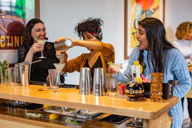 Three women having fun making cocktails in a cocktail making class