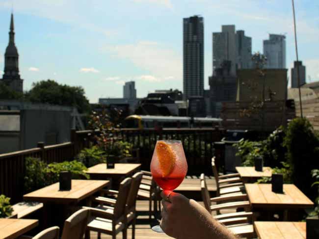 Cocktail held against a backdrop of the London skyline on the TT Roof Terrace
